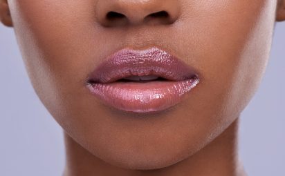 Black woman wearing a neutral pink-brown lip gloss to accentuate her lips.