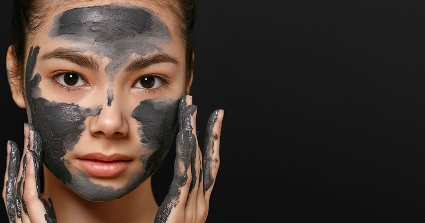 A woman is applying a charcoal face mask