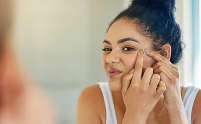 A girl looking at her acne in the mirror.