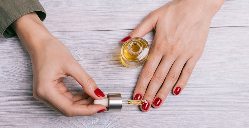An individual is applying cuticle oil to their nails
