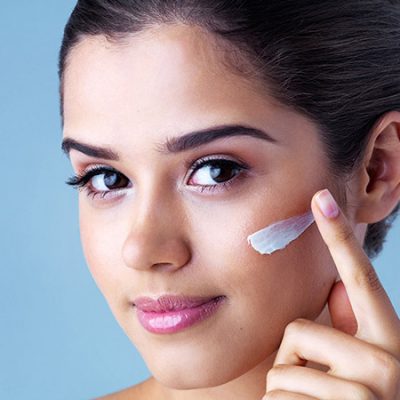 Why You Need to Have Retinol In Your Skincare Routine young woman applying face cream against a blue background