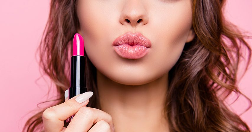 A woman is holding lipstick and puckering her lips