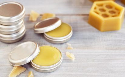 small metal tins filled with beeswax lip balm sit on a wooden surface