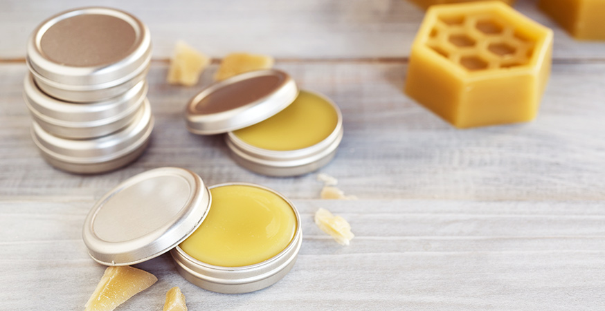 small metal tins filled with beeswax lip balm sit on a wooden surface