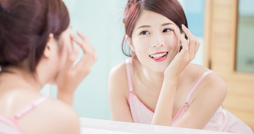 asian woman touching eyelashes while looking in mirror