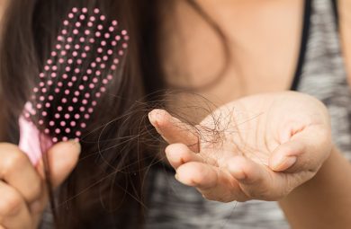 woman holding a hair brush in one hand and strands of loose hair in the other