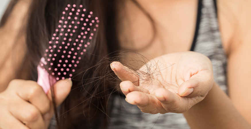 woman holding a hair brush in one hand and strands of loose hair in the other