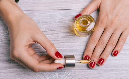 woman with red painted finger nails putting oil on cuticles