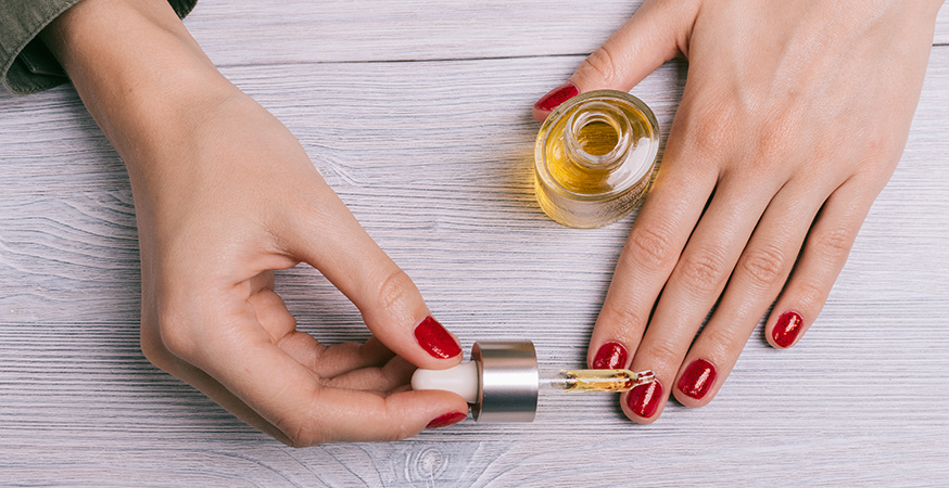 woman with red painted finger nails putting oil on cuticles