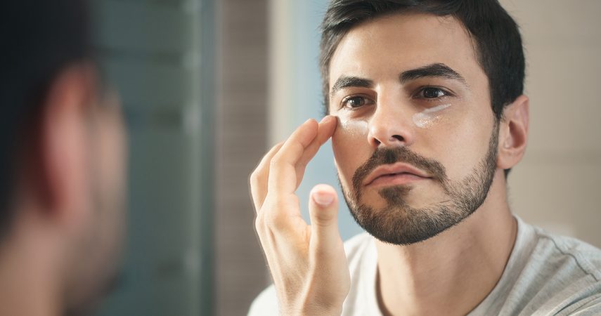 man applying cream under eyes