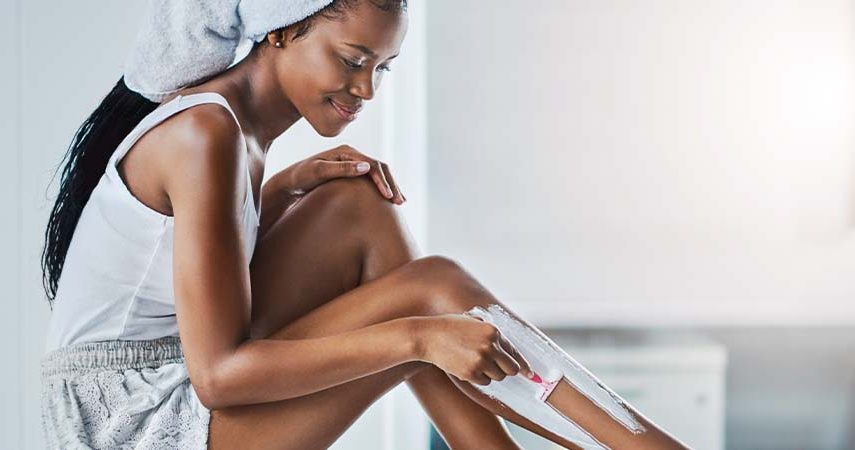A woman in a bathroom shaving her legs.