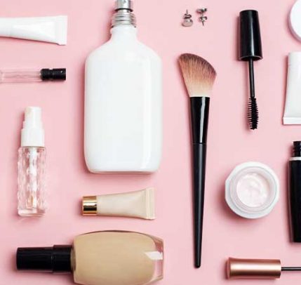 Perfume, makeup brushes and foundation against a pink background.