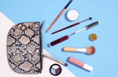 A picture of an open makeup bag with different makeup and makeup tools spread out in front of it.