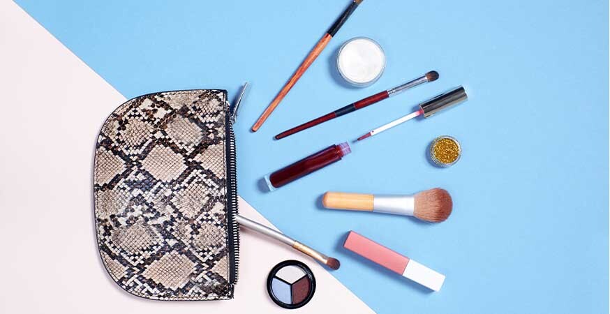A picture of an open makeup bag with different makeup and makeup tools spread out in front of it.