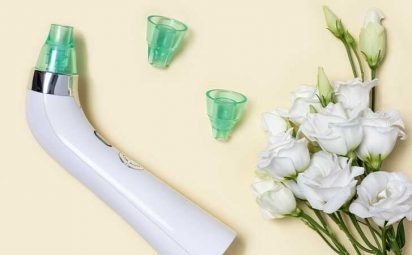 An image of a blackhead suction tool with two replacement tips laying next to white flowers.