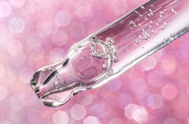 A tube of serum in front of a pink, sparkly background.