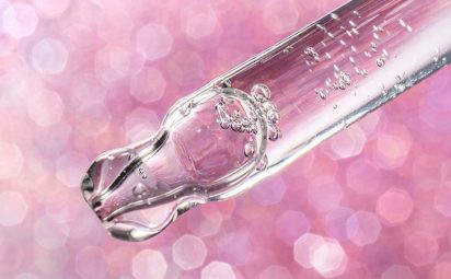 A tube of serum in front of a pink, sparkly background.
