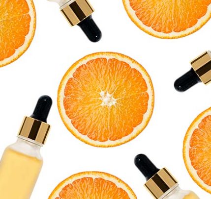 Slices of oranges with bottles of vitamin C serum against a white background.