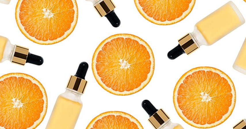 Slices of oranges with bottles of vitamin C serum against a white background.